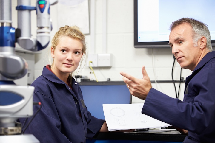 Engineer Showing Trainee Plans With CMM Arm In Foreground